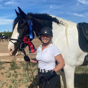 Online student Carole posing with her horse with a first and second place rosettes pinned to her horse.